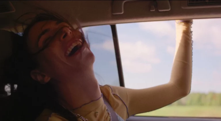 A person sitting in a car smiling with their arm out the window