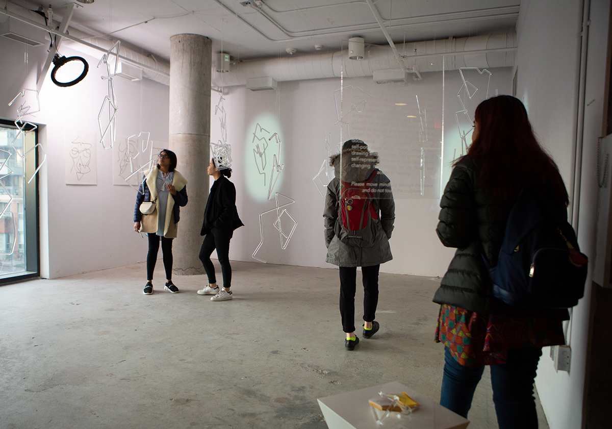 Four people standing in a white room with plexiglass tube structures hanging from the ceiling.