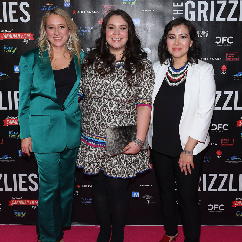 An image of three ladies standing side by side on the red carpet, taking a photo together.