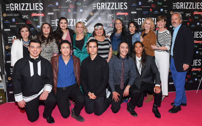A group photo of a cast and crew on a red carpet.
