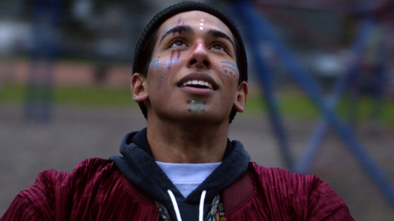 A young man with glittery paint on his face, looks up towards the sky