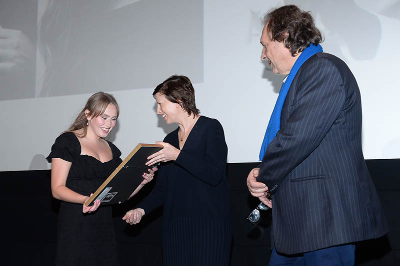 A young woman on stage accepting an award from two individuals.