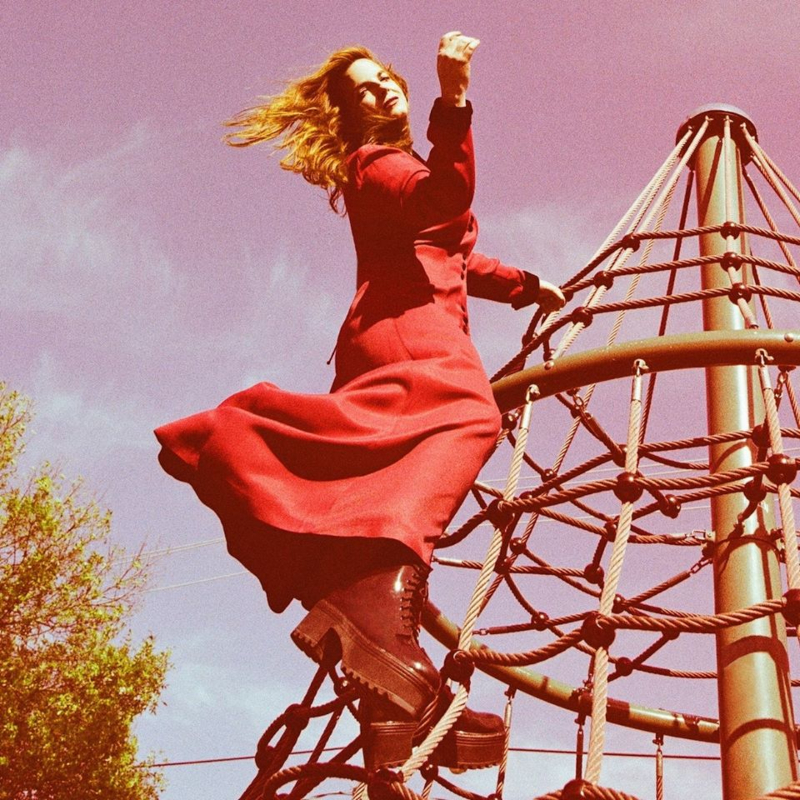 A woman in a red dress poses at the top of a rope climbing structure