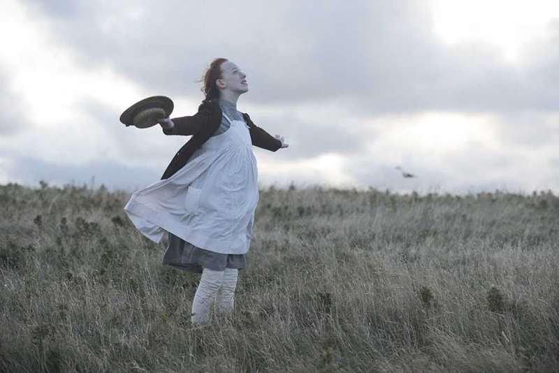 A young girl stands in a field of grass with her arms spread open