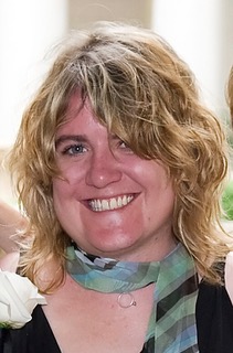 A portrait of a woman smiling with blonde hair wearing a green scarf tied around her neck