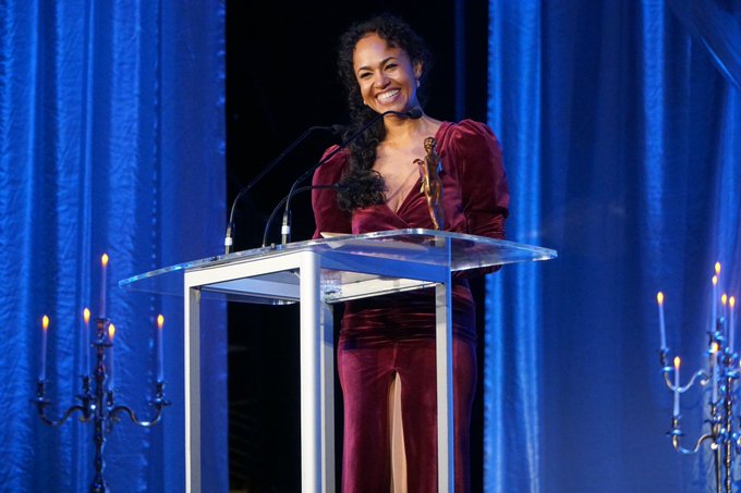 A woman stands at a podium and smiles as she accepts an award