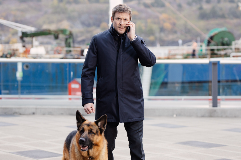 A man walks while holding and talking on his cell phone, his german shepherd walks him