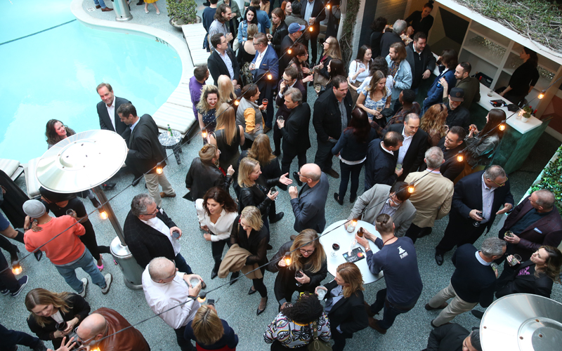 A shot of a crowd that is enjoying cocktails by a pool for an event.