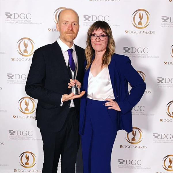A man and a woman pose for a picture with an award in their hands in front of a step and repeat