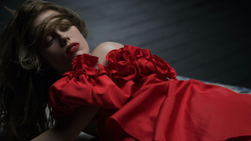 A woman wearing a red dress and red lipstick lies down and looks back 