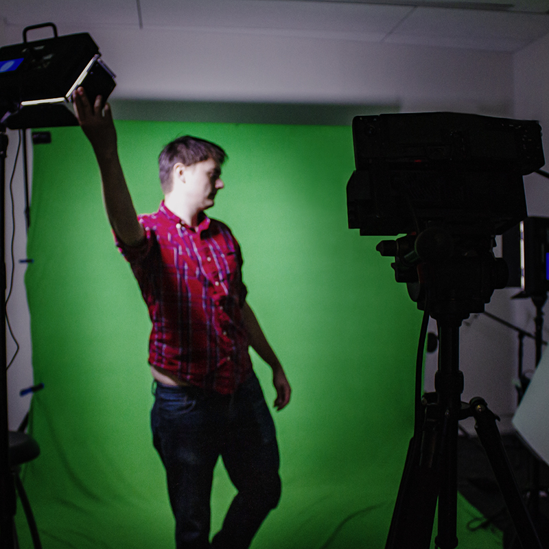 A man setting up stereoscopic-volumetric capture technology in front of a green screen.