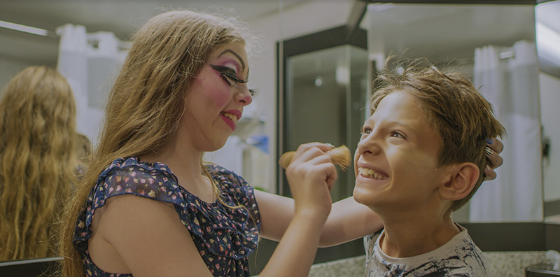 Two children help each other prepare for a performance by applying makeup.