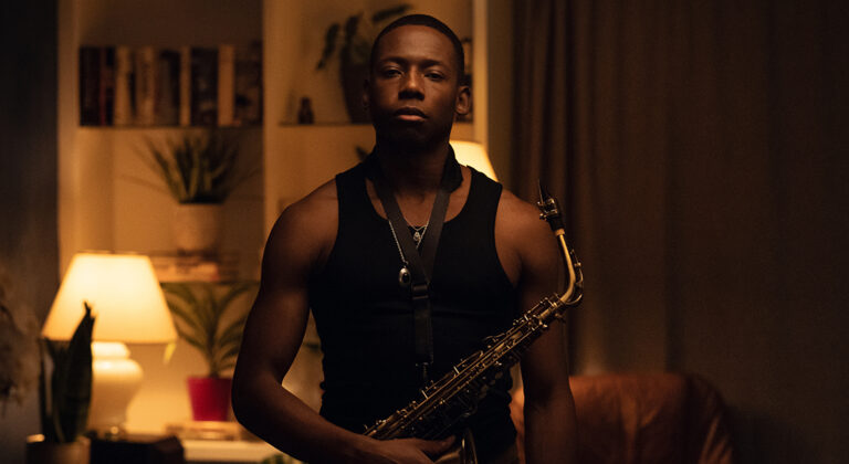 A man in a black tank top holding a saxophone