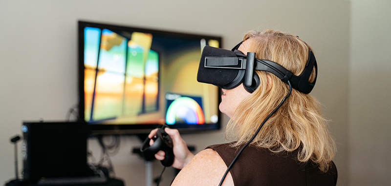 A woman in a VR headset, with a TV screen blurred out in the background.