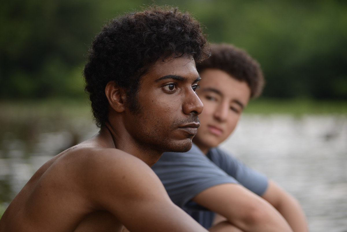 A picture of two young men sitting on a beach; the closer one in focus, the father one out of focus